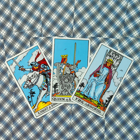 Tarot kortos Rider–Waite, trys Kardų kortos (Riteris, Karalienė, Karalius) išdėstytos kampu ant mėlyno languoto fono