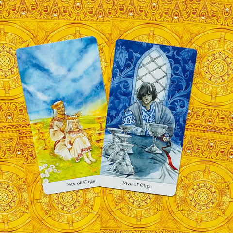 Taro kortos rinkinyje atviros Six of Cups ir Five of Cups kortos ant geltono ornamentuoto fono, pabrėžiančios praeities šilumą ir gedulą