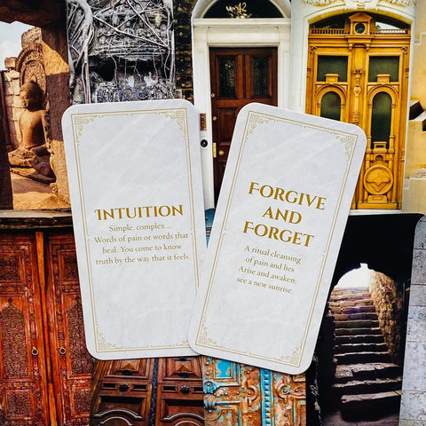 Orakulo kortos baltu marmuro fone su auksiniu tekstu, dvi išskleistos kortos „Intuition“ ir „Forgive and Forget“, fotografuota iš viršaus ant durų koliažo