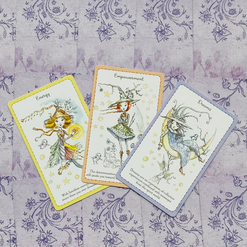 Orakulo kortos rinkinys — trys kortos (Energy, Empowerment, Dreams) su geltonu, oranžiniu ir violetiniu apvadu ant rausvo‑violetinio fono