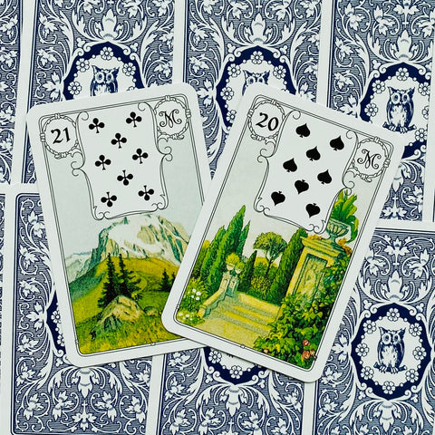 Lenormand kortos, dvi atverstos kortos (21 Kalnas, 20 Sodas) su baltais rėmeliais ant mėlynų nugarėlių, rodoma iliustracijų detalė