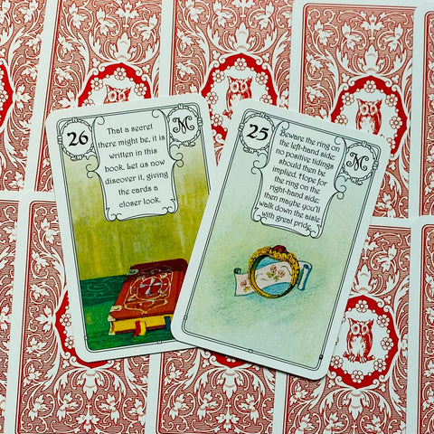 Tarot kortos, atvertos dvi kortos (knyga ir žiedas) ant raudonų nugarėlių, parodytos artimo plano.