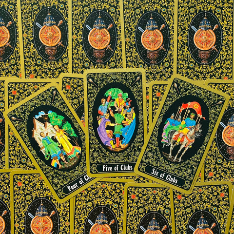 Tarot kortos juodo su aukso raštu nugarėmis, trys detalios figūrinės kortos (Four, Five, Six of Clubs) matomos