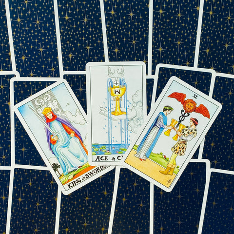 Tarot kortos Rider–Waite stiliumi, trijų kortų išklotinė: Karalius kardų, Puodelių tūzas ir Dviejų puodelių kortos ant tamsiai mėlynos žvaigždėtos nugarėlės