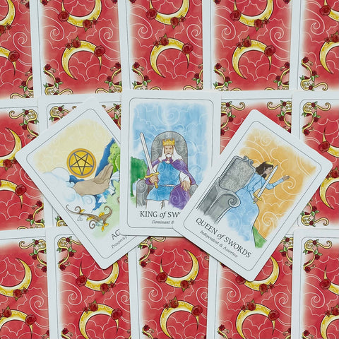 tarot kortos su raudonomis nugarėlėmis ir aiškiais iliustruotais paveikslais — Kardų karalius, Kardų karalienė ir Monetų tūzas matomi iš viršaus