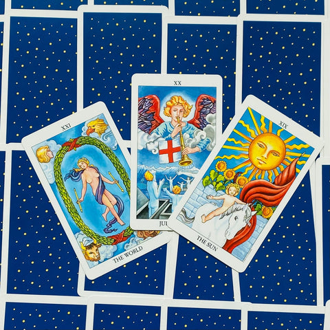 tarot kortos Rider‑Waite stiliaus, trys atverstos kortos (The World, Judgement, The Sun) ant mėlynų nugarėlių su auksinėmis žvaigždėmis