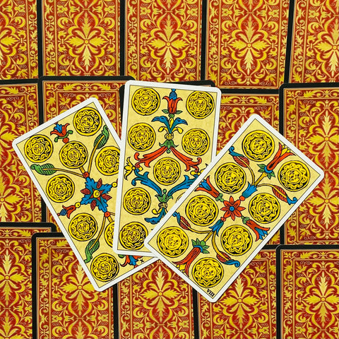 Tarot kortos — trys išskleistos monetų rūšies kortos su geltonais ornamentais ir raudonomis auksuotomis nugarėlėmis