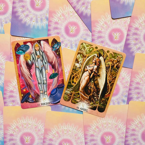 Tarot kortos – dvi atviros angelų kortos (Rikbiel ir Ariel) ant pastelinio rožinio–melsvo nugarėlių fono, kolekcijos dizaino variantas