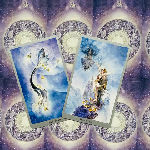 Tarot kortos – dvi taurų kortos (Eight ir Seven of Cups) mėlyno akvarelinio dizaino, priekis ir violetinis galinis raštas matomi