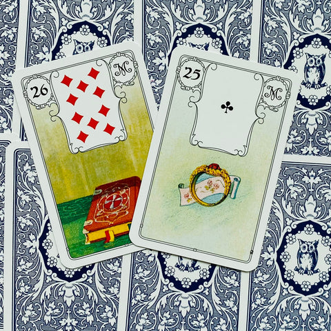 Lenormand kortos su atverstomis 26 (knyga) ir 25 (žiedas) kortomis ant mėlyno nugarėlių rašto, sudėtos diagoniškai