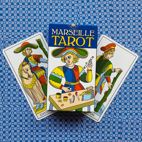 Marseille taro rinkinys su dėžute priekyje ir trimis klasikinėmis kortomis ant mėlyno raštuoto audinio