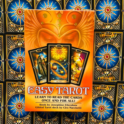 Easy Tarot mokomoji knyga su oranžiniu viršeliu ir Ciro Marchetti gilded taro kortomis, per vidurį trys kortos (The Sun), fone pasikartojantis kortų raštas