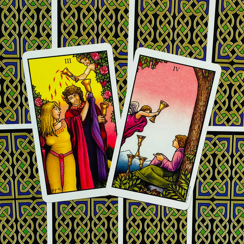 Tarot kortos Rider‑Waite stiliaus, atvertos III ir IV taurės priekinės pusės, matomas keltiškas juodai‑žalias nugarėlių raštas