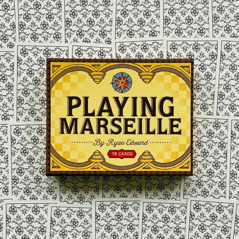 Kortos Playing Marseille geltoname dėkle (78 kortų), priekiniu kampu centre ant išklotų nugarėlių, skirtos klasikinėms taro partijoms