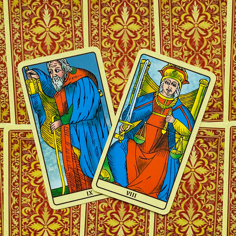 tarot kortos Marseille stiliaus, dvi kortos (IX ir VIII) ryškiai mėlynos ir raudonos, atsidengusios ant raudono ornamentuoto fono