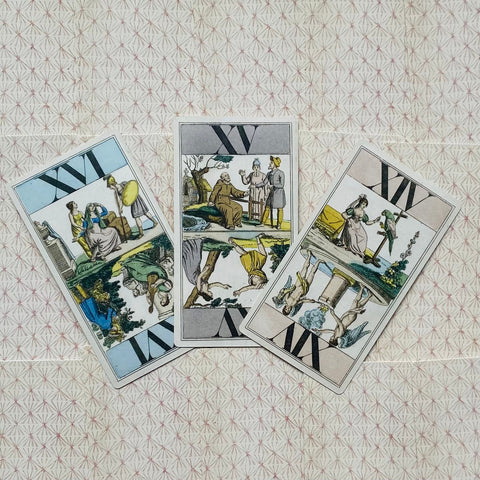 Tarot kortos retro dizaino rinkinio trys kortos ant raštuoto fono, išdėstytos pasvirai — dvi apverstos, viena stačia