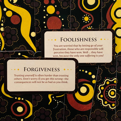 Orakulo kortos, artimas planas: dvi kortos (Foolishness ir Forgiveness) ant juodo‑geltono ornamentuoto fono