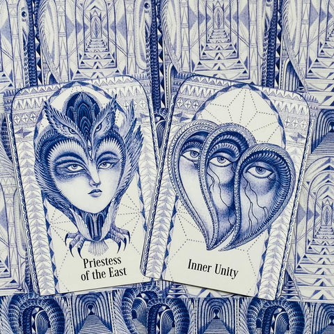 Tarot kortos su mėlynomis pieštinėmis iliustracijomis, arti matomos dvi kortos (Priestess of the East, Inner Unity) ir detalus raštas