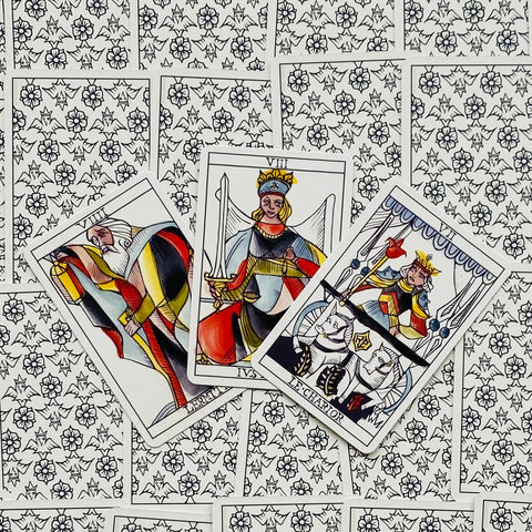Tarot kortos su spalvingais didžiųjų arkana piešiniais, trijų kortų išdėstymas ant baltai juodo gėlių ir širdžių rašto