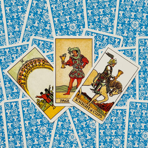 Tarot kortos Rider‑Waite stiliaus su mėlynomis nugarėlėmis, trys atvertos Taurių kortos (X, Puslapis, Riteris) centre