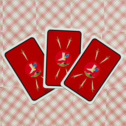 tarot kortos su ryškiai raudonomis nugarėlėmis, trijų kortų vėduoklės išdėstymas ant rožinio raštuoto fono