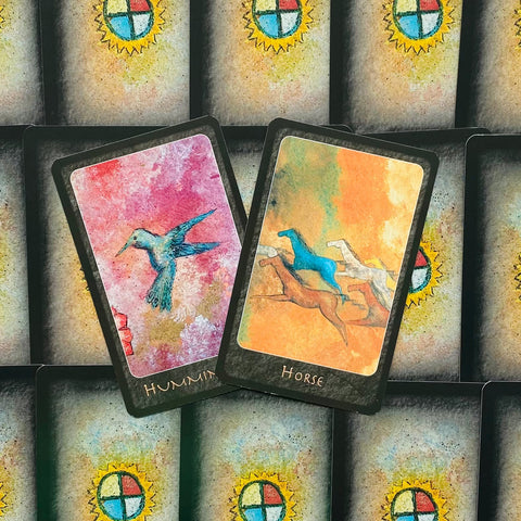 Tarot kortos su spalvotomis iliustracijomis — atverstos kolibrio ir arklio kortos virš nugarėlių su saulės simboliu