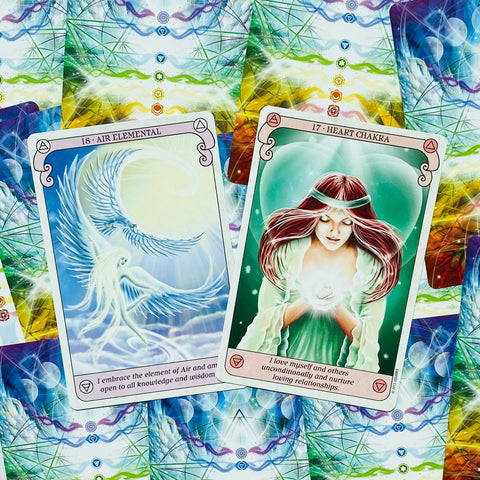 Orakulo kortos: matomos priekinės Air Elemental (mėlyna) ir Heart Chakra (žalia) kortos, fone – spalvingas nugarėlių raštas, skirtas parodyti dizainą ir variantus