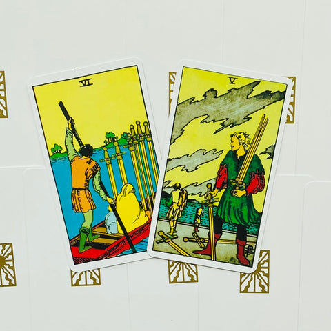 tarot kortos Rider‑Waite komplektas, priekyje Penki ir Šeši kalavijų kortos, šiek tiek persidengiančios ant baltos dekoruotos dėžutės