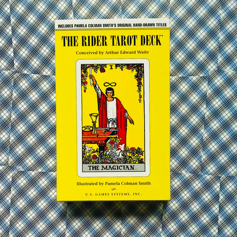 Rider Tarot Deck geltona dėžutė su The Magician korta priekyje, frontinis kampas ant mėlyno raštuoto audinio