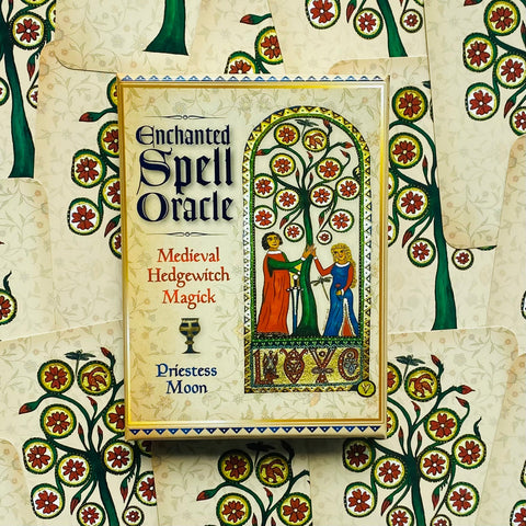 Orakulo kortos Enchanted Spell Oracle, Priestess Moon dėžutė kremine viršutine dalimi ir žalios‑raudonos medžių ornamentikos kortų fone