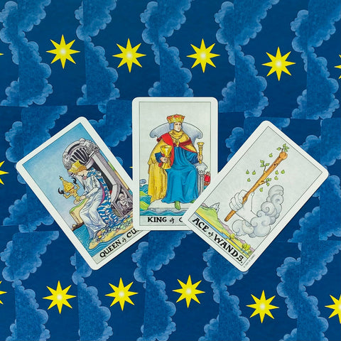 Tarot kortos tris kortų išdėstymas: Queen of Cups, King of Cups ir Ace of Wands ant mėlyno žvaigždėto audinio, skirtas skaitymui