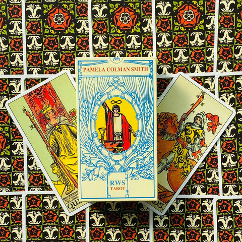 RWS tarot kortos Pamela Colman Smith baltame dėkle centre, dvi atverstos kortos šone ant ornamentuoto fono