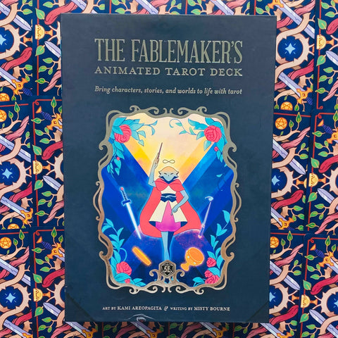 Produkto puslapis — The Fablemaker's Animated Tarot juoda frontalinė dėžutė su spalvotu kortų iliustracijos rėmu ir raštuotu fonu