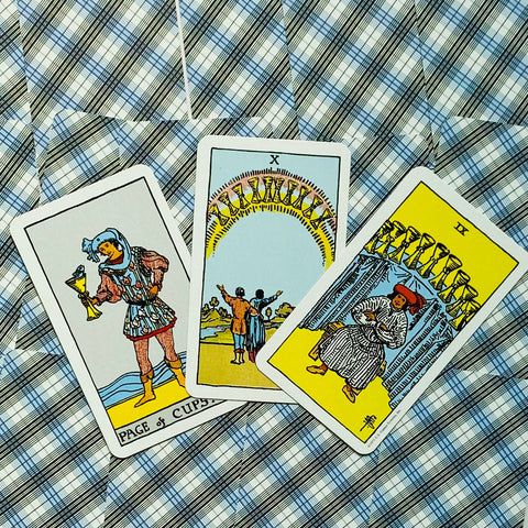 Tarot kortos Rider‑Waite stiliaus, trys atverstos taurų rūšies kortos ant mėlyno pledo fono, artimas planas
