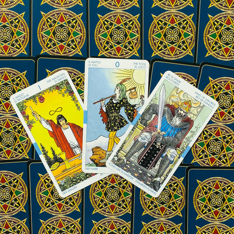 Tarot kortos — trys atverstos Didžiosios Arkos kortos (Magas, Kvailys, Kardų karalius) ant mėlynos nugarėlės su auksiniu ornamentu