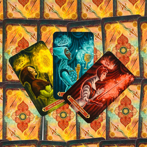 Tarot kortos — trys karalienės (pentaklių, taurių, lazdų) geltonos, mėlynos ir raudonos iliustracijos, išskleistos centre ant dekoratyvių nugarėlių