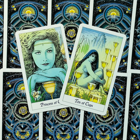 tarot kortos su mėlyno‑juodo kosminio rašto nugarėlėmis, centre dvi atviros kortos kampu (Princess of Cups, Ten of Cups)