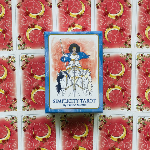Simplicity Tarot kortų rinkinys mėlynoje dėžutėje (Emilie Muñiz), padėtas ant raudonų kortų nugarėlių su mėnulio ir rožių raštais