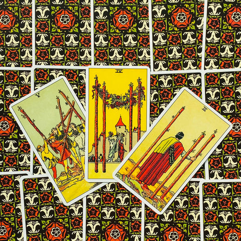 Tarot kortos Rider–Waite, trijų lazdelės kortos išdėstytos ant juodai-raudonai raštuotos nugarėlės, arti fotografuota