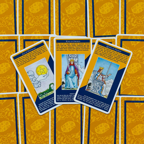Tarot kortos su geltoniomis ir mėlynomis nugarėlėmis, plokščiai išdėliotos ir atverstos centrinėse Kardų ir Monetų kortose, pabrėžia šio dizaino variantą