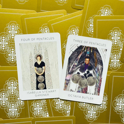 Tarot kortos su auksinėmis ornamentuotomis nugarėlėmis, dvi atvertos kortos (Three of Pentacles, Four of Pentacles) matomos