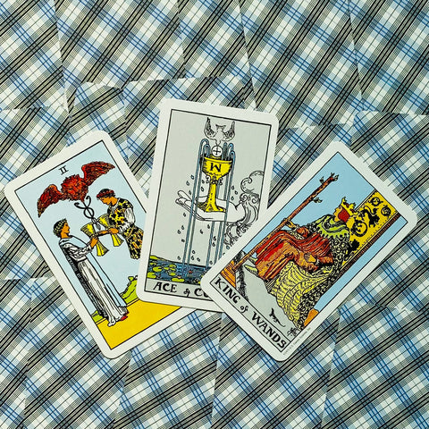 Tarot kortos atverstos trimis kortomis — Dviejų taurės, Taurių tūzas ir Lazdų karalius — plokščias išdėstymas ant mėlyno languoto fono
