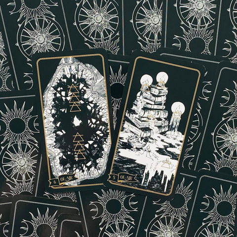 Tarot kortos juodo fono su auksiniais raižiniais, dvi atvertos kortos iš viršaus, matomas unikalus nugarėlės saulės raštas
