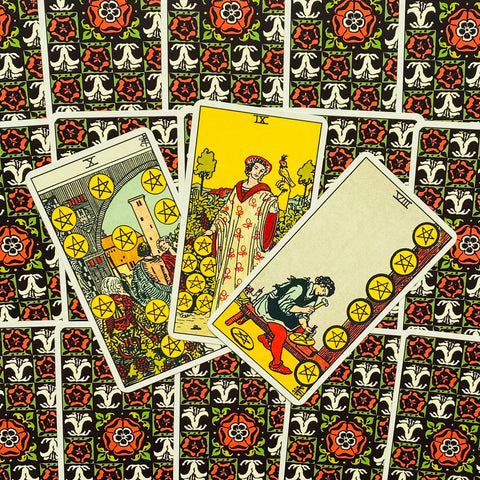 Tarot kortos Rider‑Waite komplektas, trys pentaklio kortos išdėliotos iš fanerio ant juodai‑raudono raštuoto nugarėlių fono