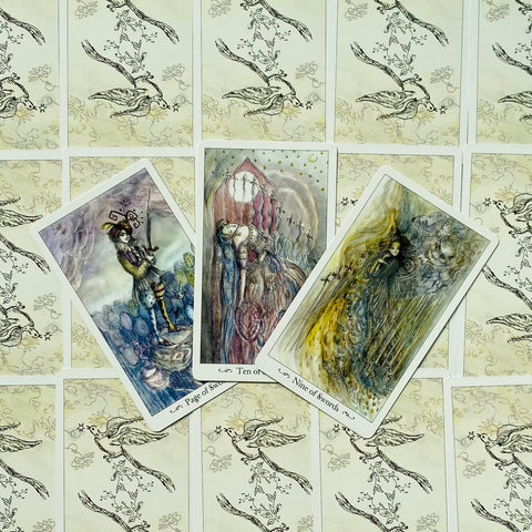 Tarot kortos – trys atverstos kortos (Puslapis, Dešimt ir Devynios kalavijai) su smulkiais akvareliniais piešiniais, parodytos priekiniu dizainu