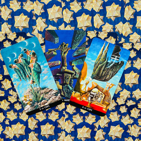 Tarot kortos – trijų kortų rinkinys (5 of Cups, 6 of Cups ir Wands) išdėstytas ant mėlynos žvaigždžių rašto, detalus kampo kadras
