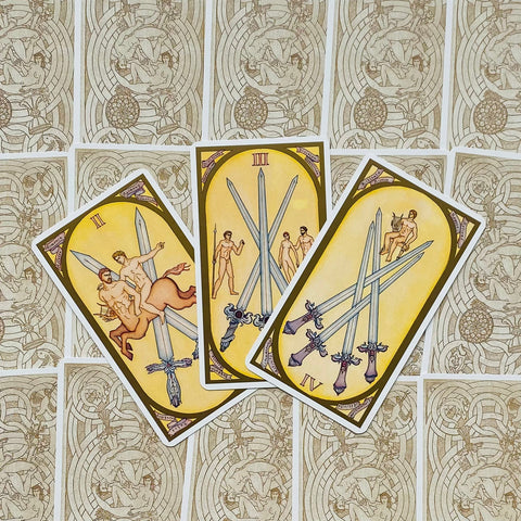 tarot kortos geltonomis kortomis: trys kardų (II–IV) kortos fanuotos ant ornamentuotos nugarėlės fono
