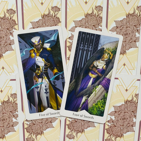 Tarot kortos, iliustruotos mėlyno‑violetinio ir aukso spalvų, dvi kardų kortos (Five/Four of Swords) ant gėlių nugarėlių, artimas produktų varianto kadras