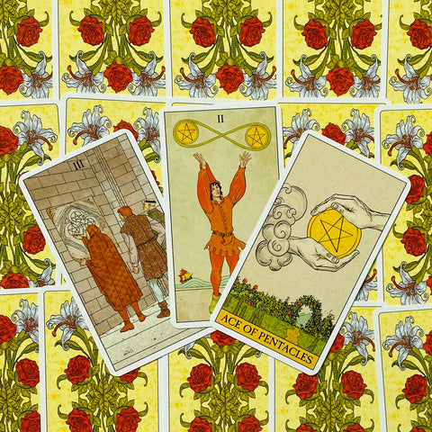 tarot kortos RWS stiliaus komplektas — trys atvertos kortos (Ace of Pentacles, II, III) ant geltonos rožių nugarėlės
