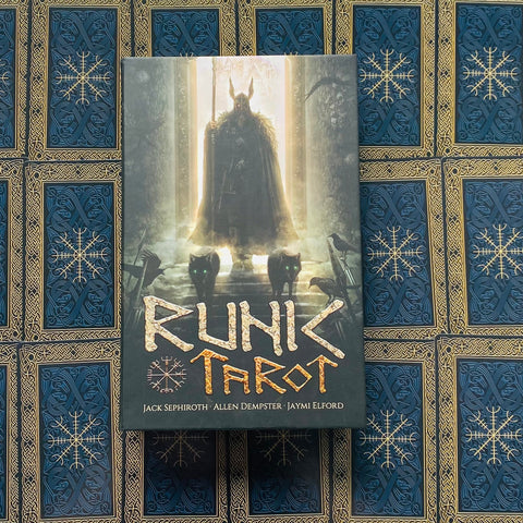 Runų tarot dėžutė su vikingų figūra ir dviem žaliai žibančiomis katėmis, padėta centriniu kampu ant mėlyno aukso ornamentuoto fono